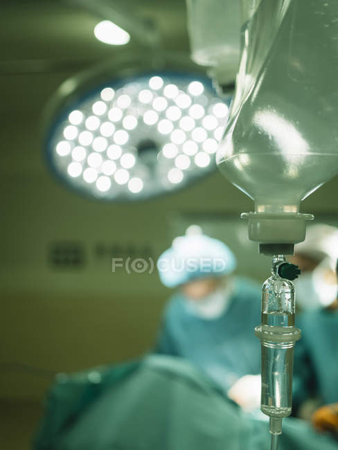 Drop bottle over blurred surgeons — Stock Photo