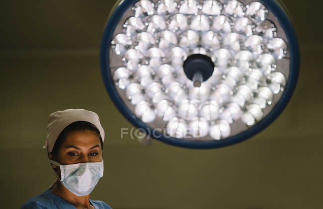 Feminino médico vestindo máscara de pé sobre a lâmpada — Fotografia de Stock