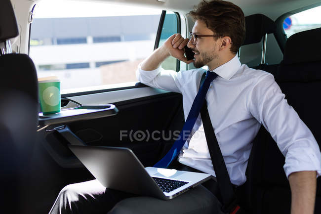 Homme avec ordinateur portable parlant au téléphone dans la voiture — Photo de stock