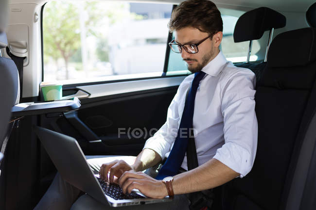 Hombre de negocios que trabaja con el ordenador portátil en coche - foto de stock