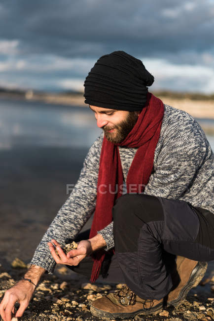 Sorridente maschio raccogliendo ciottoli a riva — Foto stock