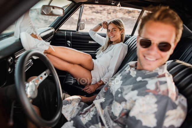 Jovem alegre olhando para a câmera posando no carro enquanto cavalga com o namorado — Fotografia de Stock