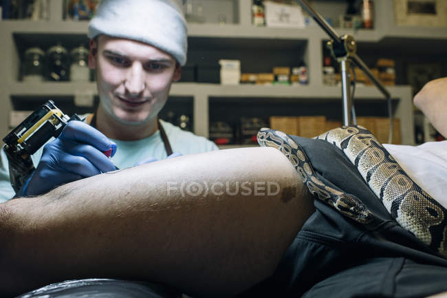 Mestre tatuagem perna enquanto grande cobra deitado sobre ele — Fotografia de Stock