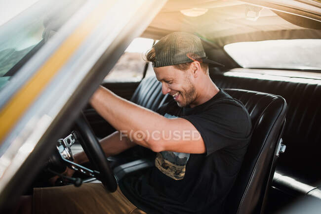 Веселий молодий чоловік сидить в машині і запускає двигун Горизонтальний постріл на відкритому повітрі — стокове фото