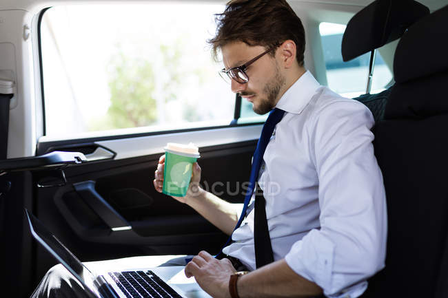 Homme avec café et ordinateur portable en voiture — Photo de stock
