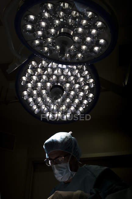 Хирург в маске работает под лампой — стоковое фото