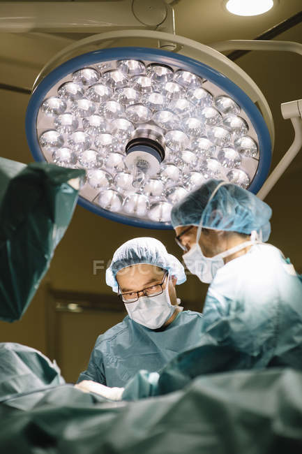 Surgeons under bright lamp and providing operation — Stock Photo