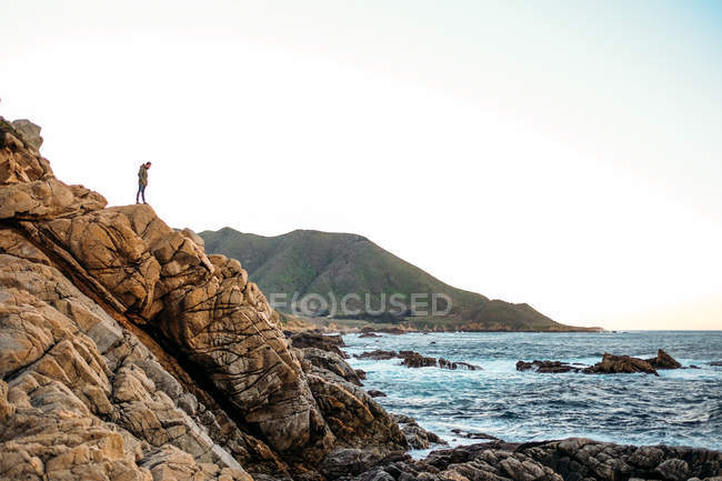 Masculino em pé no penhasco e admirando a paisagem aquática — Fotografia de Stock