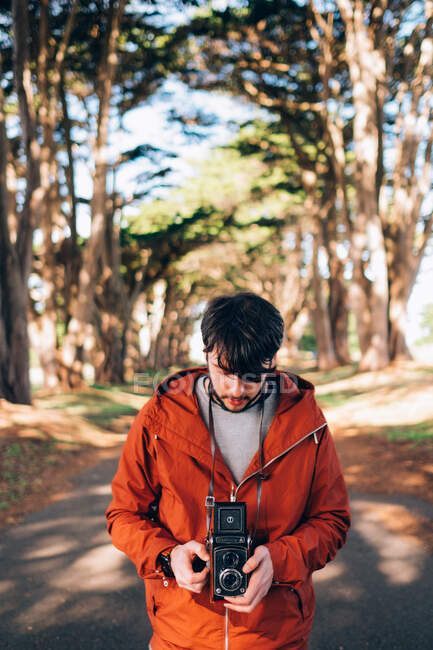 Портрет людини, що стоїть на лісовій дорозі і тримає старовинну фотокамеру — стокове фото