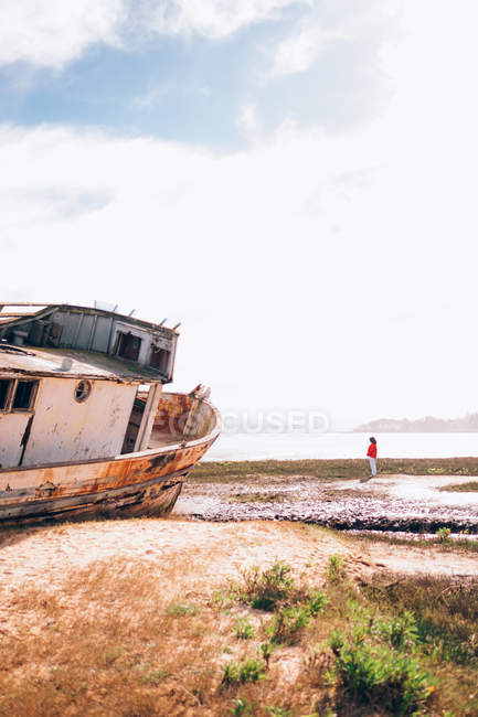 Girl standing by abadoned ship on shore — Stock Photo