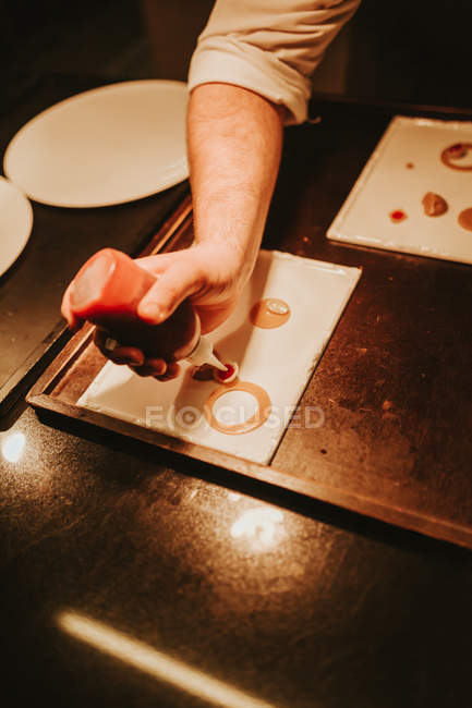 Cooks hand decorating plates by sauce — Stock Photo