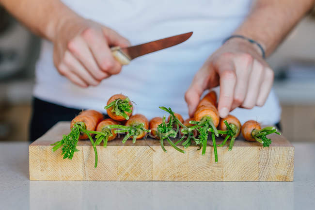 Mãos com faca cortando cenouras — Fotografia de Stock