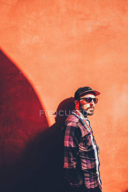 Homem posando na parede vermelha iluminada pelo sol — Fotografia de Stock