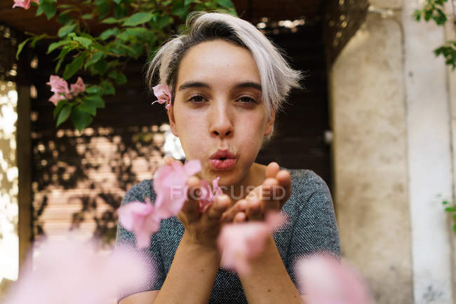 Woman blowing petals from hands — Stock Photo