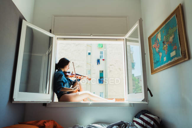 Романтична жінка грає на скрипці на підвіконні — стокове фото