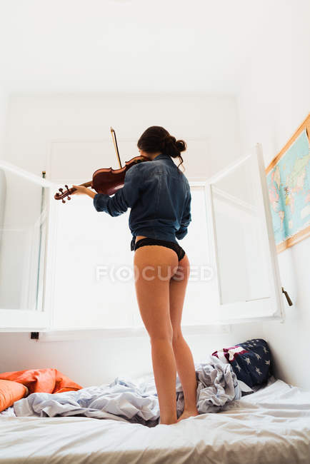Femme sexuelle jouant du violon sur le lit — Photo de stock