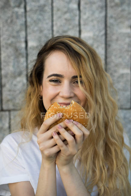 Ragazza sorridente mangiare hamburger — Foto stock