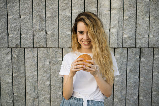 Ragazza sorridente mangiare hamburger — Foto stock