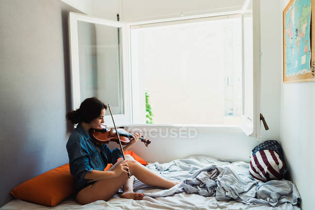 Mujer tocando el violín en la cama - foto de stock