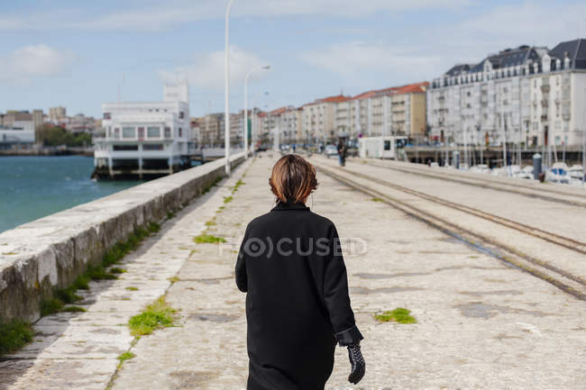 Anonymous woman in black walking at waterfront — Stock Photo