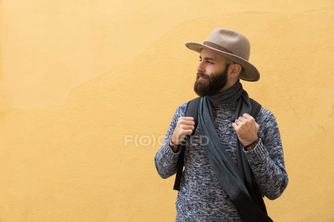 Бородатий чоловік з рюкзаком позує на жовтій стіні і дивиться в сторону . — стокове фото