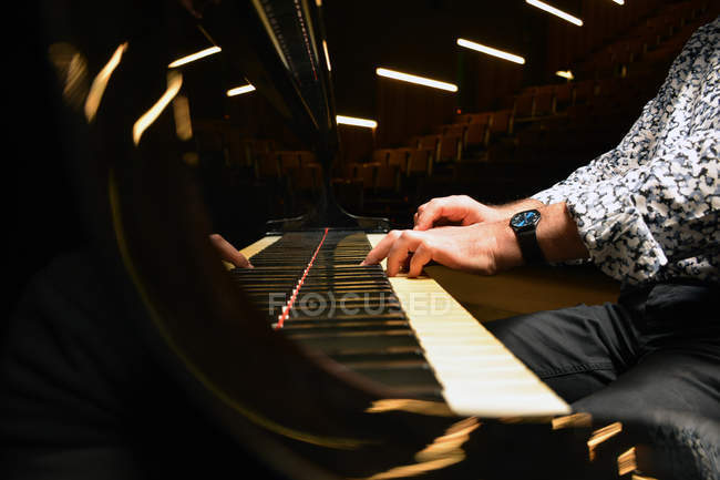 Мужские руки корпуса играют на фортепиано на фоне пустого зала — стоковое фото