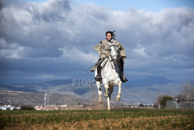 Frontansicht einer Frau, die auf einem laufenden Pferd auf einem Feld reitet — Stockfoto