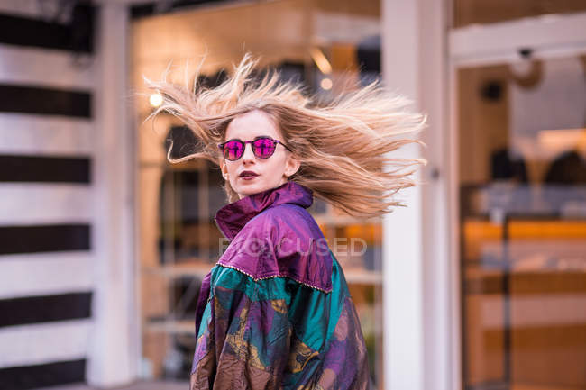 Menina elegante nova em óculos de sol olhando para trás sobre o ombro com o cabelo acenando . — Fotografia de Stock