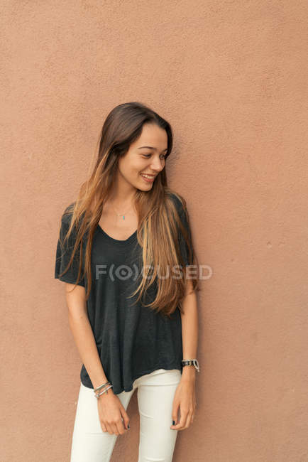 Ritratto di ragazza sorridente che posa contro il muro marrone e distoglie lo sguardo . — Foto stock
