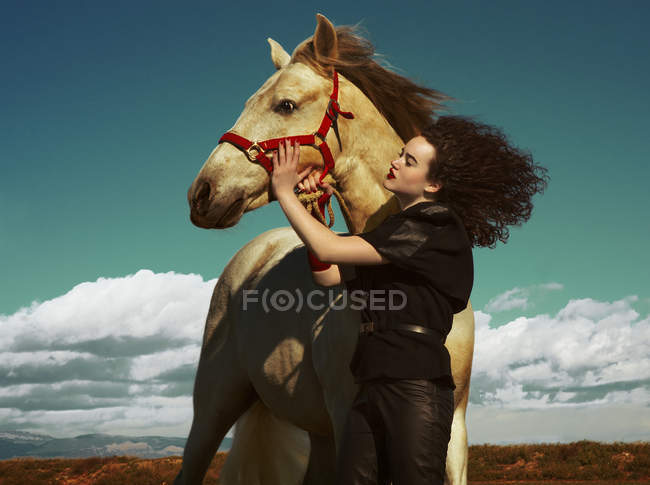 Jovem segurando cavalo no fundo do campo — Fotografia de Stock