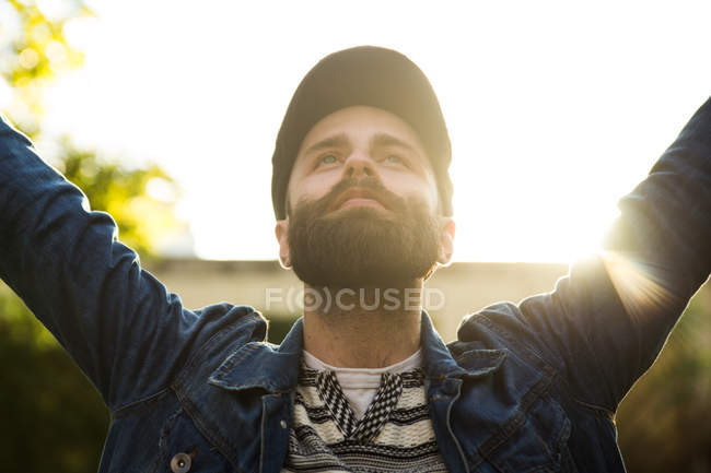 Porträt eines Mannes in Mütze und Jeansjacke, der die Hände in die Höhe hält und glücklich aussieht. — Stockfoto