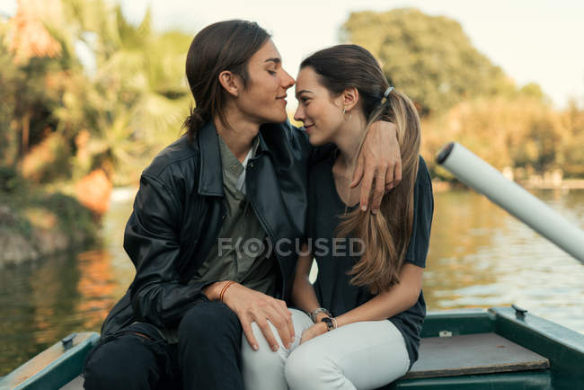 Ritratto di ragazzo seduto su barca e abbracciando ragazza al lago del parco — Foto stock