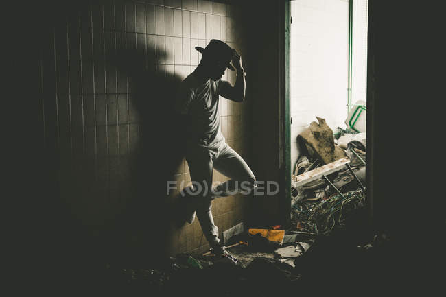 Elegante hombre apoyado en la pared en habitación abandonada con montones de basura
. - foto de stock
