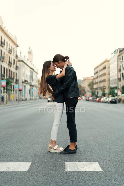 Vista lateral de pareja joven abrazándose en la carretera en la escena de la calle - foto de stock