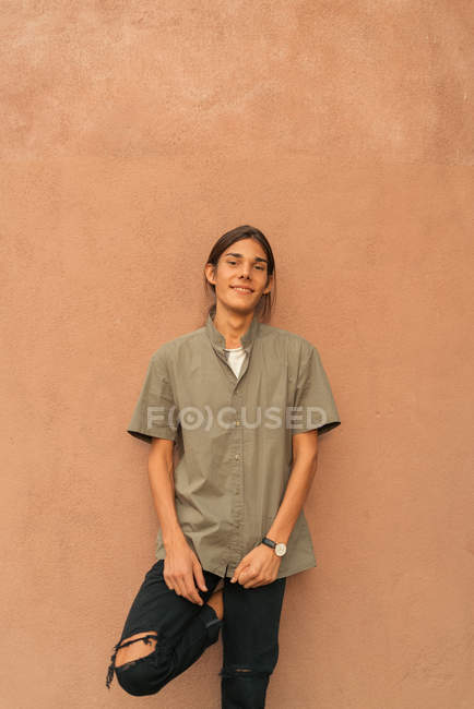 Porträt eines brünetten langhaarigen Jungen, der sich an die Wand lehnt und in die Kamera blickt — Stockfoto