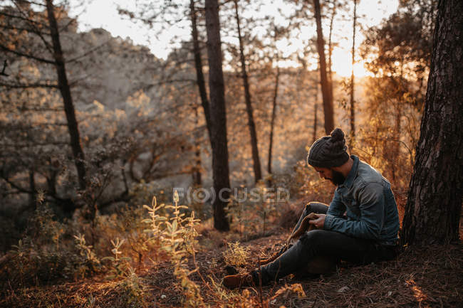 Человек сидит в лесу и смотрит в рюкзак — стоковое фото