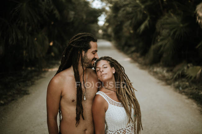 Retrato de menina com dreadlocks inclinando-se sobre o homem sem camisa no beco tropical — Fotografia de Stock