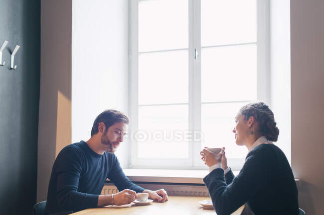 Jovens adultos bonitos sentados no café e conversando enquanto bebem café. — Fotografia de Stock