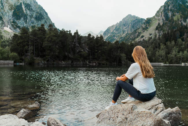 Woman sitting on stone at lake — Stock Photo