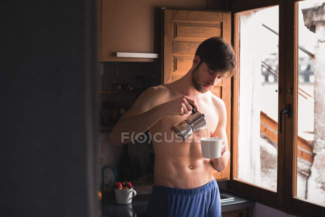 Hombre en topless llenando una taza con café en la cocina . - foto de stock