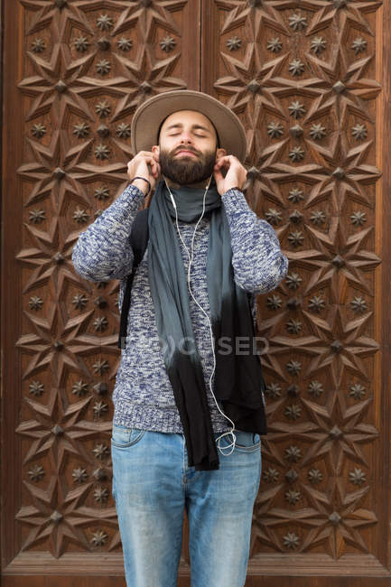 Портрет бородатого человека, затыкающего наушники с закрытыми глазами над декоративной барельефной дверью — стоковое фото