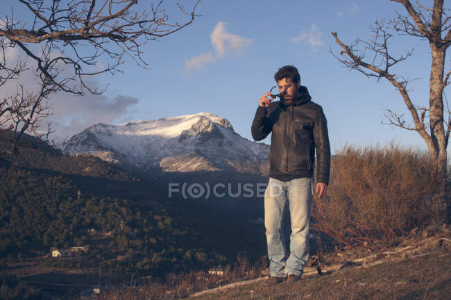 Человек в кожаной куртке в лесу холодный весенний день на фоне заснеженных гор — стоковое фото