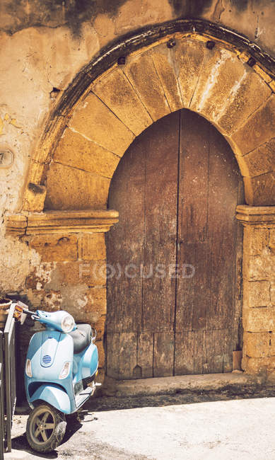 Синій скутер припаркований старими арочними дверима — стокове фото