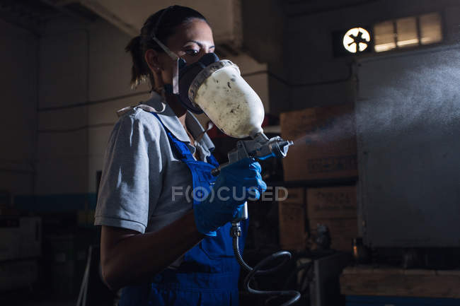 Seitenansicht einer Mechanikerin mit Atemschutzmaske und Spritzpistole — Stockfoto