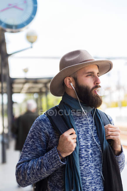 Portrait of man in hat blowing gum bubbles and listening to music at street scene — Stock Photo