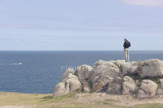 Rückansicht eines Mannes auf einem Felsen mit Blick auf das Meer an einem sonnigen Frühlingstag — Stockfoto
