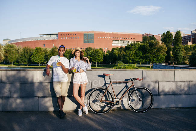 Couple avec boissons et vélo penché sur parapet — Photo de stock