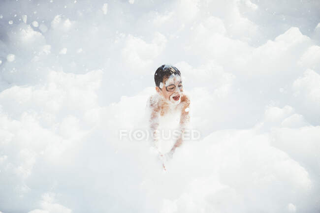 Ragazzo giocoso divertirsi in schiuma bianca ridendo felicemente. — Foto stock