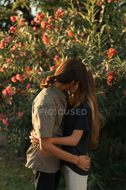 Portrait of embracing couple kissing over blooming plants on backdrop — Stock Photo