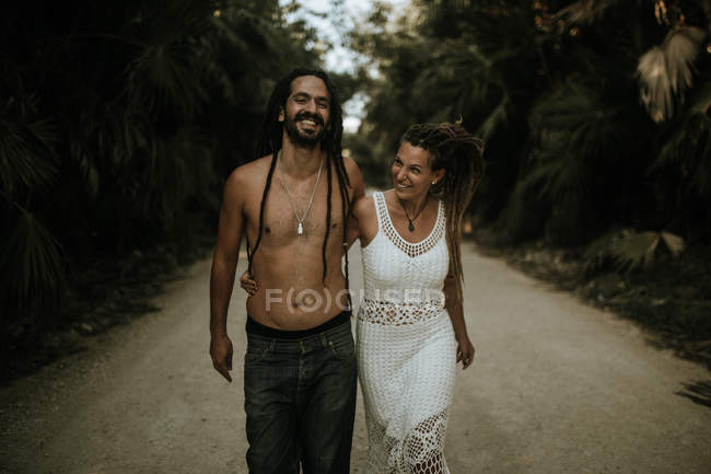 Retrato de pareja sonriente abrazando y caminando en callejón en bosques tropicales . - foto de stock